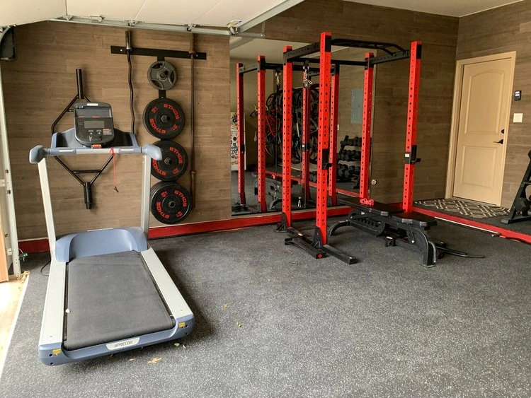 Treadmill, squat rack, and weights hung up on the wall of a custom garage gym.