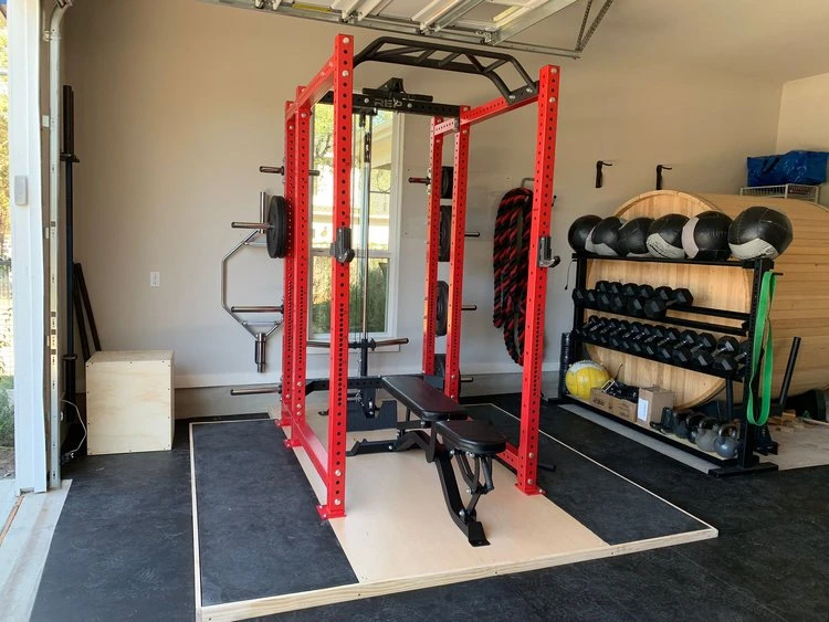 Red squat rack, medicine balls, and weights in a small garage gym.