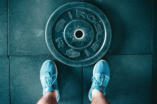 A bench press weight is laid flat on the floor with a person’s shoes touching the weight.